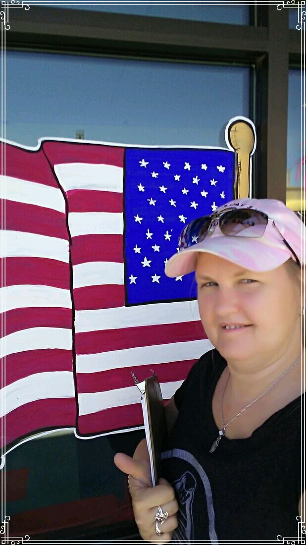 artist M Burgess standing in front of her American flag window painting